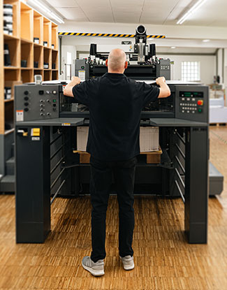 Vorreiter in Sachen Technik - Ein Mann in schwarzer Kleidung steht vor einer neuen Druckmaschine und überprüft ein Druckerzeugnis, um die Maschine richtig zu kalibrieren.