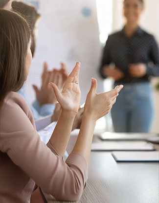 RESPEKTVOLLES MITEINANDER - Eine Schulungssituation, in der die klatschenden Kursteilnehmer rechts im Bild scharf abgebildet sind. Die unscharfe Person links neben einem Flipchart ist die Referentin.
